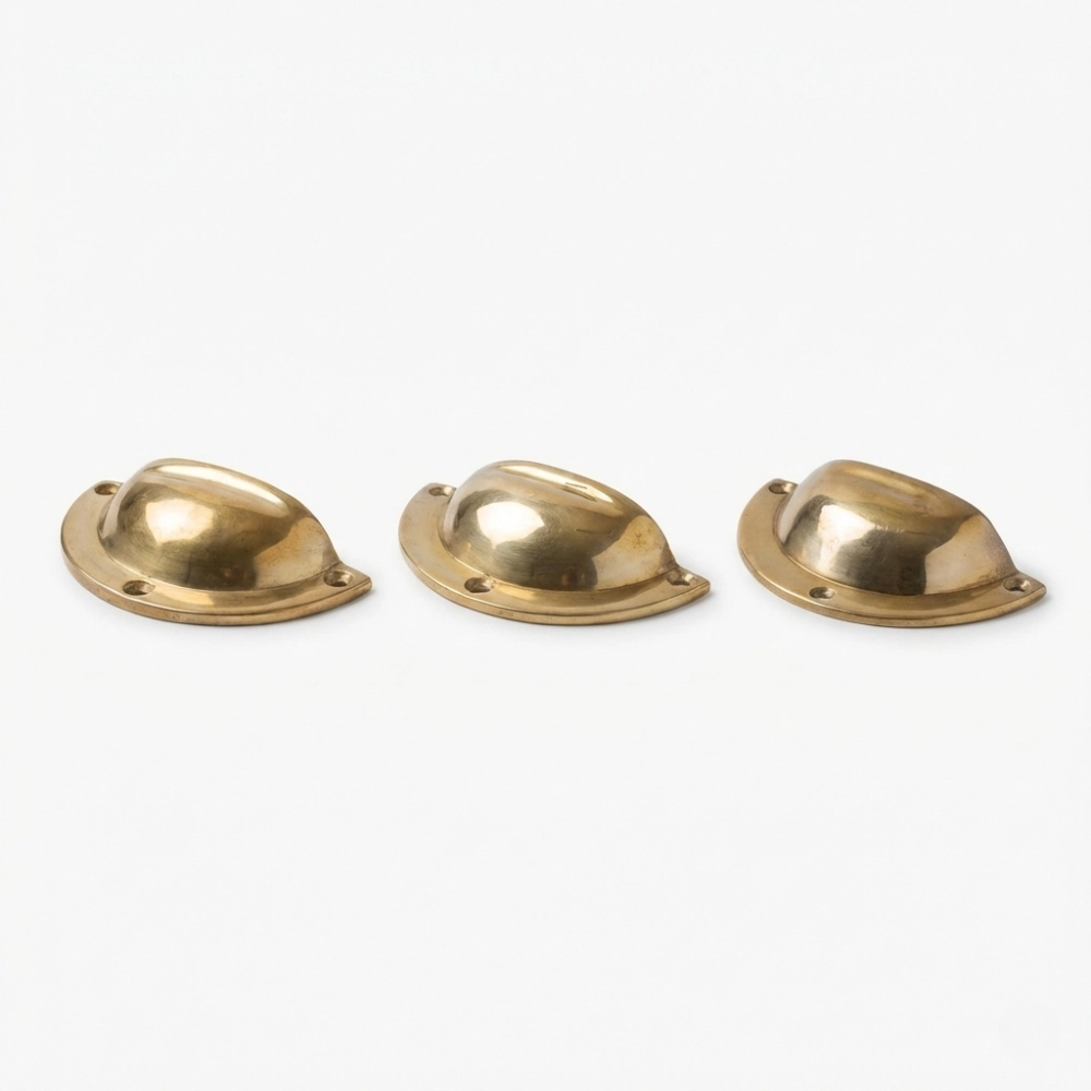 Three polished brass cup-style drawer pulls with mounting holes arranged in a row on a white background.
