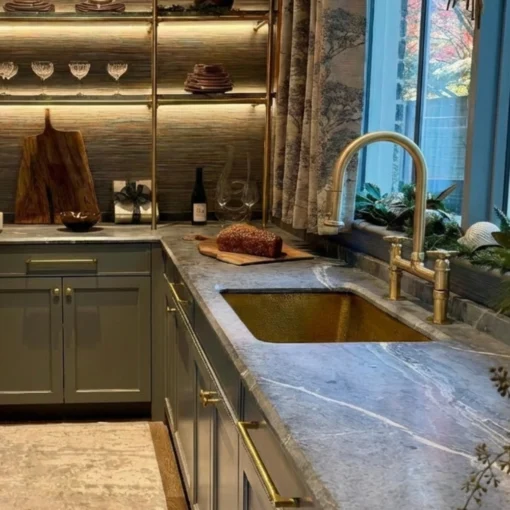 Marble countertop with gray cabinets and brass hardware, gold undermount sink and curved gold faucet.