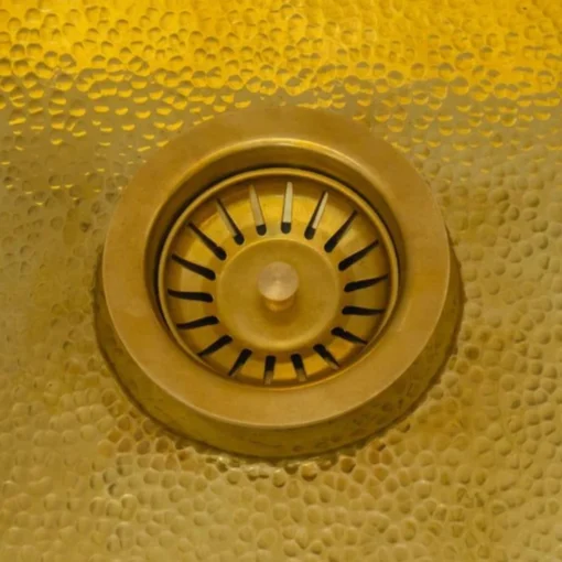 Brass sink drain strainer with a central knob set in a textured, hammered golden sink basin.