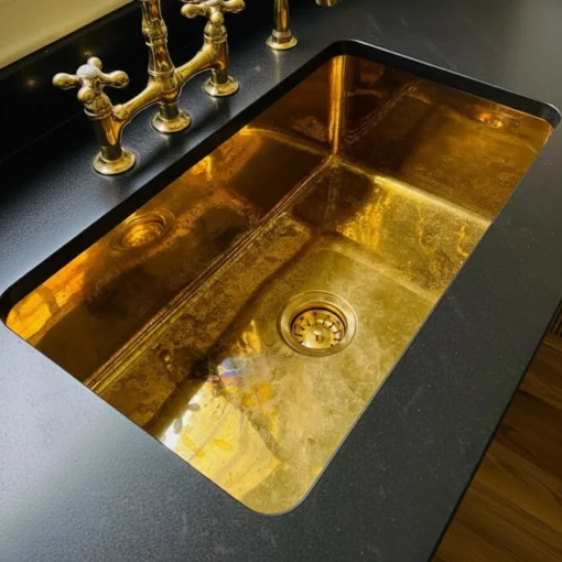brass rectangular sink with round drain and vintage-style brass faucet set in a black countertop