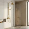 Brass rain shower with handheld spraying water in a minimalist bathroom, glass partition and shelf with bottles.