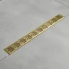 Long brass linear shower drain set in light gray tiled floor with scattered water droplets.