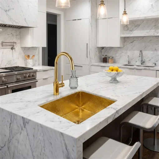 White marble kitchen island with hammered brass sink and matching gold faucet, pendant lights and a bowl of lemons.