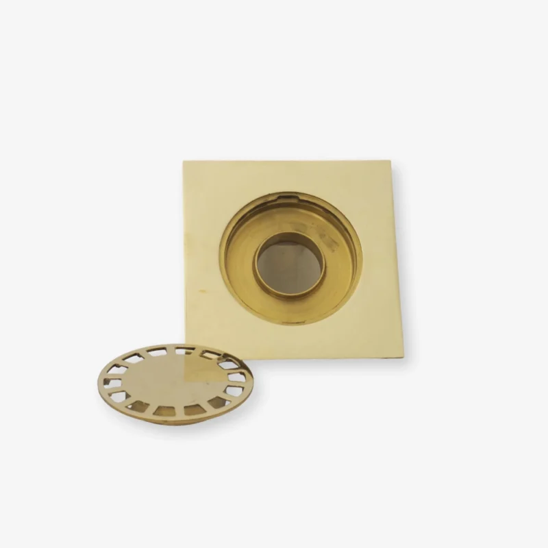 unlacquered Brass square recessed drain with a removable round perforated grate beside it on a white background.