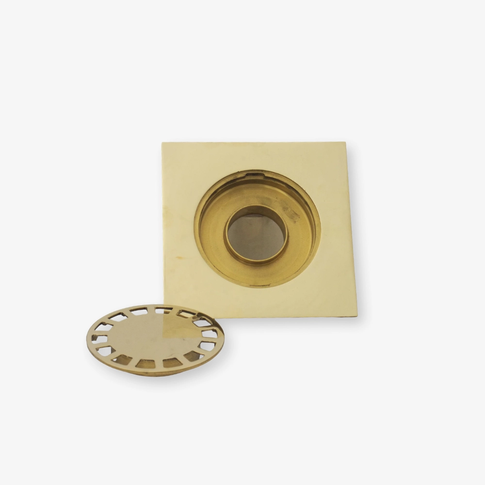 unlacquered Brass square recessed drain with a removable round perforated grate beside it on a white background.